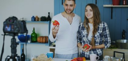 Young attractive couple recording video blog about vegetarian healthy food on dslr camera in the kitchen at home